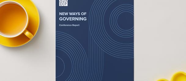 Blue booklet titled 'New Ways of Governing' on a light desk, beside a yellow mug.