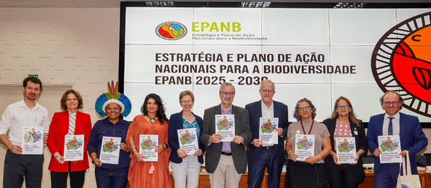People stand on stage smiling, holding certificates at biodiversity event.
