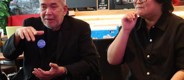 A man having a converstion in sign language with a lady on his left in a cafe.