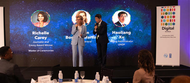 Panel discussion on a blue stage with microphones; audience in foreground.