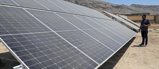 Solar panel array on desert ground with a technician standing nearby.