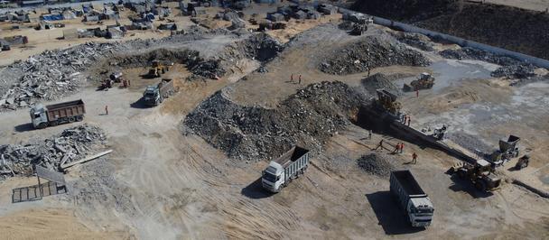 Aerial view of a dirt construction site with heavy machinery and stone walls.