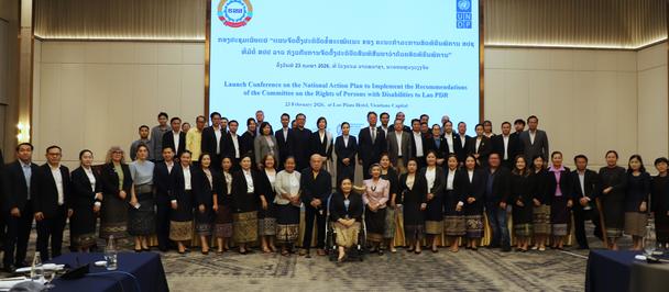 Group of professionals in formal attire posing for a conference photo with a slide presentation on screen.