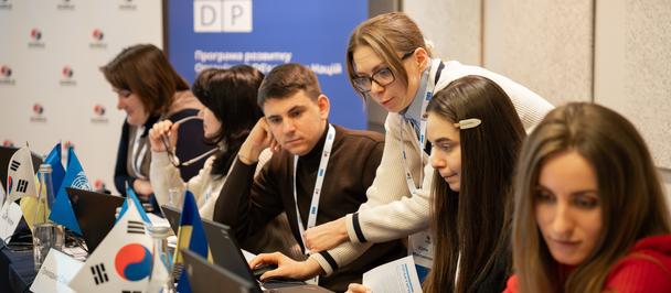 Group of people at a conference booth, working on laptops with Korean flag banners.