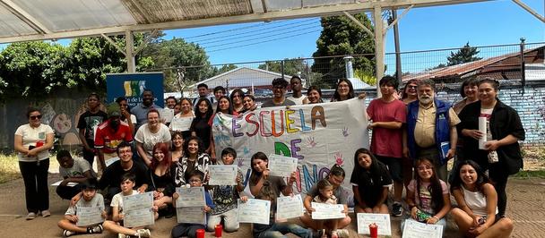 Group photo of diverse adults and children under a canopy with a colorful banner behind them.