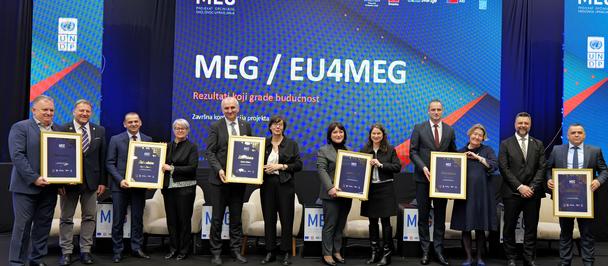 Group photo of people on stage holding framed certificates at MEG EU4MEG.