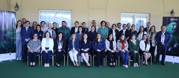 Large group of diverse professionals pose for a photo in a conference hall with a green carpet.