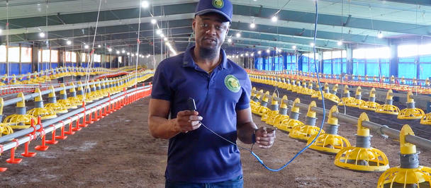 Man in blue polo and cap inside a chicken-rearing facility