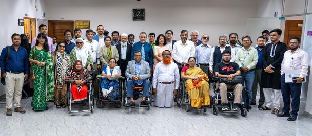 Large diverse group of people in formal attire posing for a group photo in a bright hall.