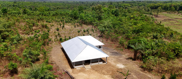 White canopy over a small shelter on a dirt field among young trees in a rural orchard.