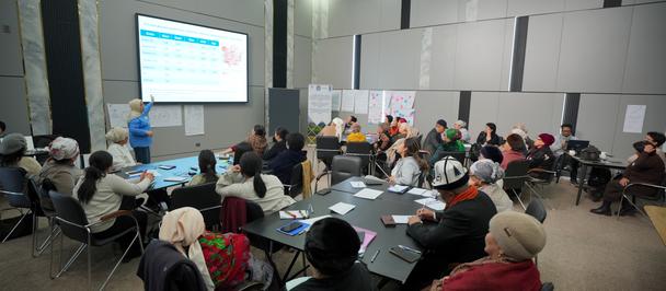 People sit around a long conference table in a bright room with a projector screen.