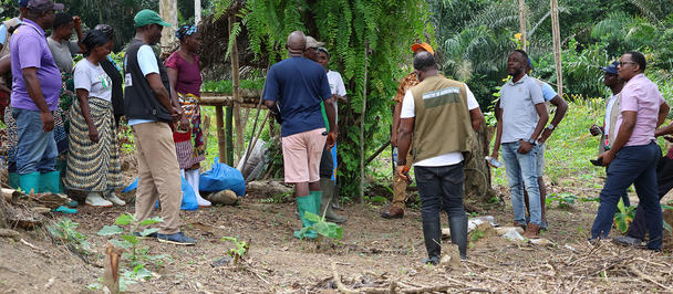 Photo of people gathered in a circle in a forested clearing.