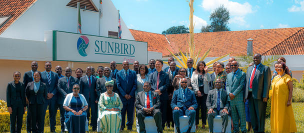 Group photo in front of a white Sunbird building with a red tile roof on a sunny day.