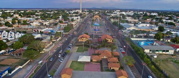 An aerial view of a wide suburban avenue with houses on both sides, palm trees, and a blue sky.