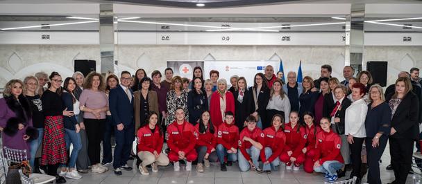 Group photograph in a hall; many people standing, several in red seated at the front.