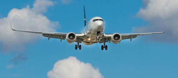 Front view of a commercial airliner approaching with landing gear down against a blue sky.