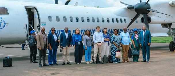 Group of people posing in front of a white twin-propeller airplane on the tarmac.