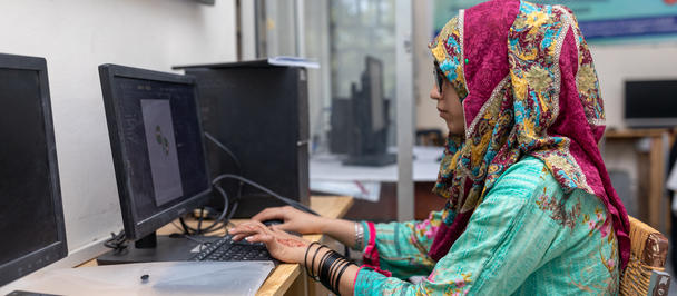 Woman in a colorful hijab using a desktop computer in a classroom.