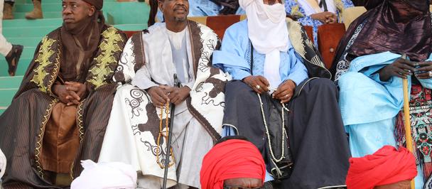 Photo of men in colorful traditional robes and turbans seated on a stage at a ceremony.