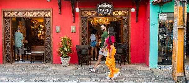 Woman in orange dress walking past a red storefront; man in doorway, potted plant nearby.
