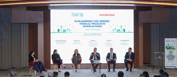 Panel discussion on stage with several speakers; audience seated in red chairs.