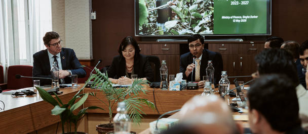 Professionals in a boardroom around a long table; a presentation screen shows a forest image.