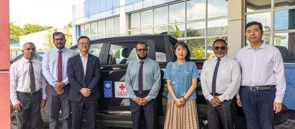Group of professionals posing outside a glass-front building with a car in the background.