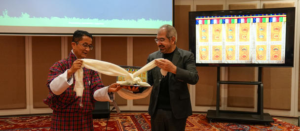 Photo of two men exchanging a white sheet in a conference room.