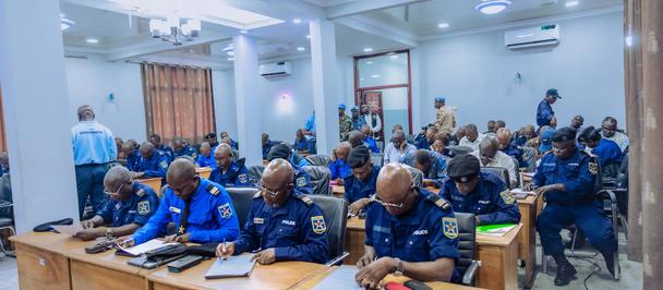 Photo: Group of people in blue uniforms seated at desks in a bright conference room.