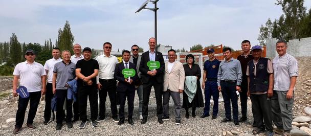 Group of people posing on rocky ground outdoors with a wind turbine behind them.
