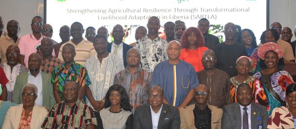 Large group of diverse attendees posing for a group photo at a conference, banner behind.