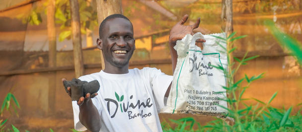 Smiling man in a white t-shirt on a farm holding a bag and a spray bottle.