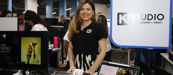 Smiling woman in black at a tech expo booth with laptops and a K Studio sign.