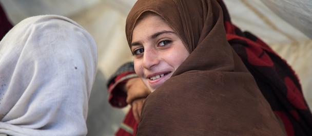 Photograph of two people wearing hijabs under a white canopy, facing away; gray and brown hijabs.