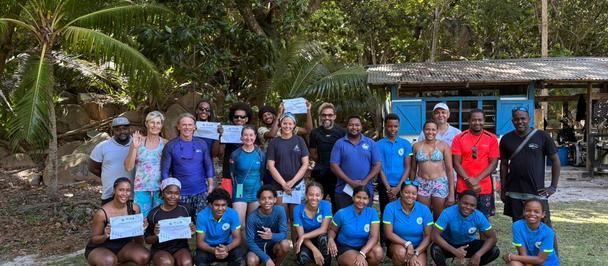 Group of people in blue shirts posing outdoors in a tropical palm-filled setting.