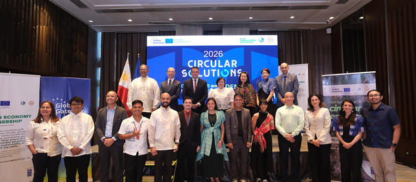 Photograph of a diverse group posing on a conference stage in front of a blue banner.