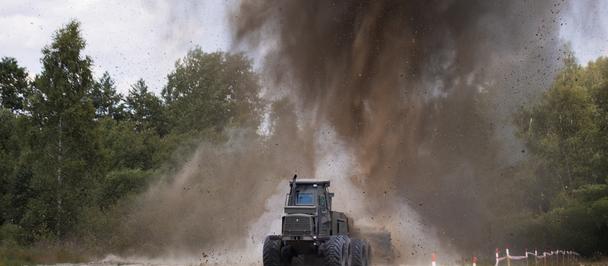 Blue heavy construction vehicle on a dusty dirt road, kicking up a large dust plume.