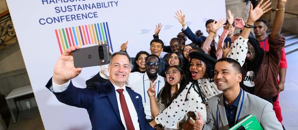 Diverse group at Hamburg Sustainability Conference posing for a photo; front man in a suit smiles.