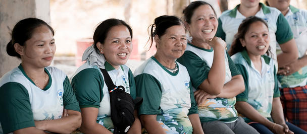 Group of smiling people in teal uniforms sitting in a row, with a small black dog on someone's lap.