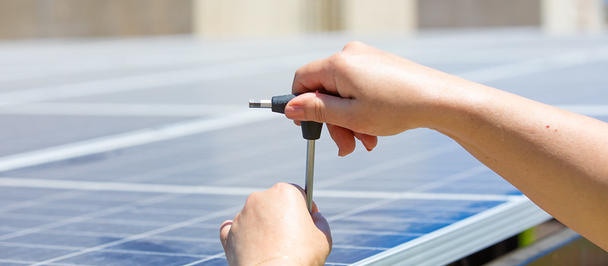 Photo of hands securing a solar panel with a screwdriver.