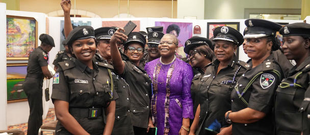 Photograph: group of uniformed officers posing with a woman in a purple dress indoors.