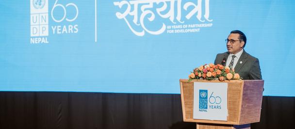 Photograph of a man in a suit at a podium on stage with a blue backdrop showing UNDP 70 years logo.