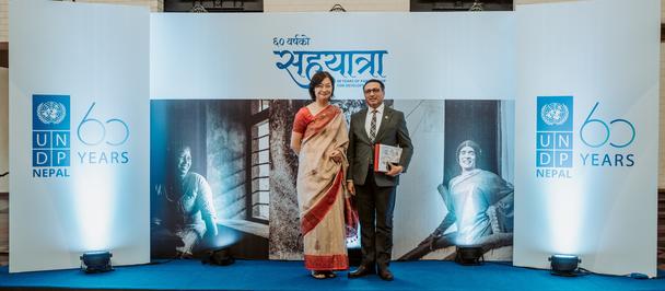 Two people stand on a stage in front of a blue backdrop with banners celebrating 200 years.