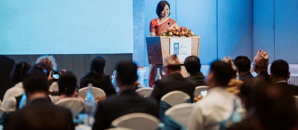 Photo: woman presenting at a podium on a blue stage to conference attendees.