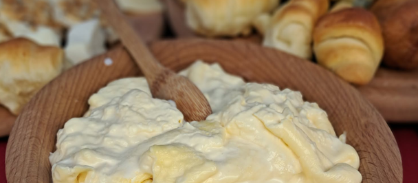 Wooden plate with a large dollop of pale whipped cream, bakery rolls in the background.
