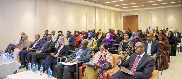Audience seated in a well-lit conference room for a seminar; front row in suits.