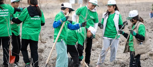 Photo: volunteers in green vests and white hard hats with shovels at a dirt field.