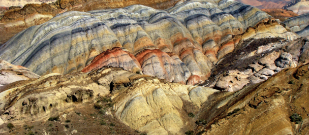 Desert landscape with colorful layered badlands, striped hills, and distant mountains.