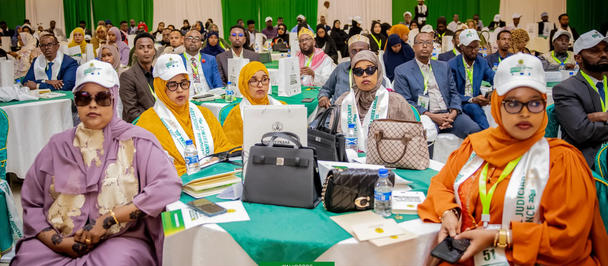 Dignitaries in colorful robes seated at a conference with banners in the background.