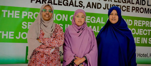 Three women in hijabs pose together in front of a vibrant green workshop banner.